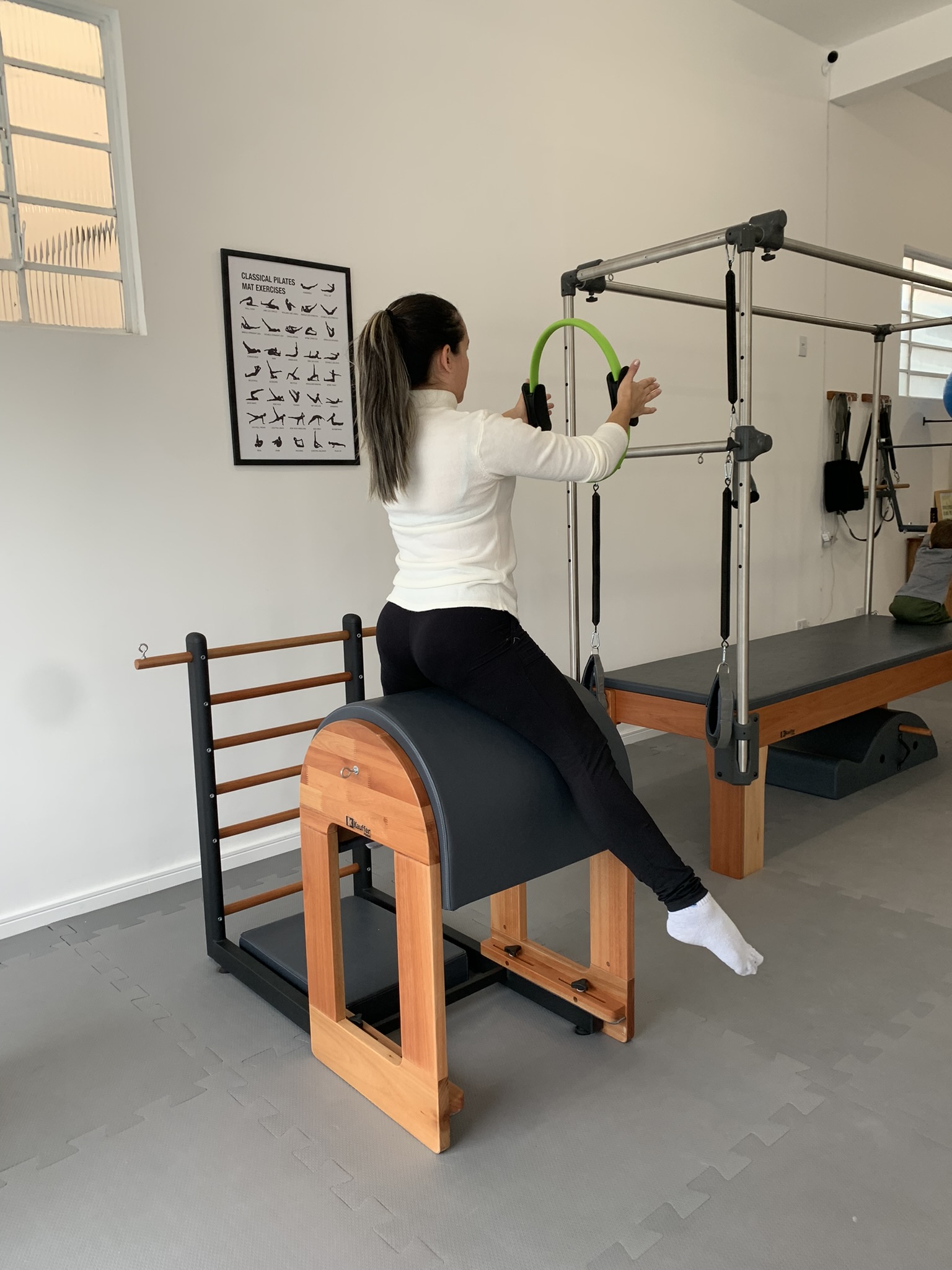 Aluna sobre ladder barrel com magic circle, trabalhando postura e alongamento em aula de Pilates