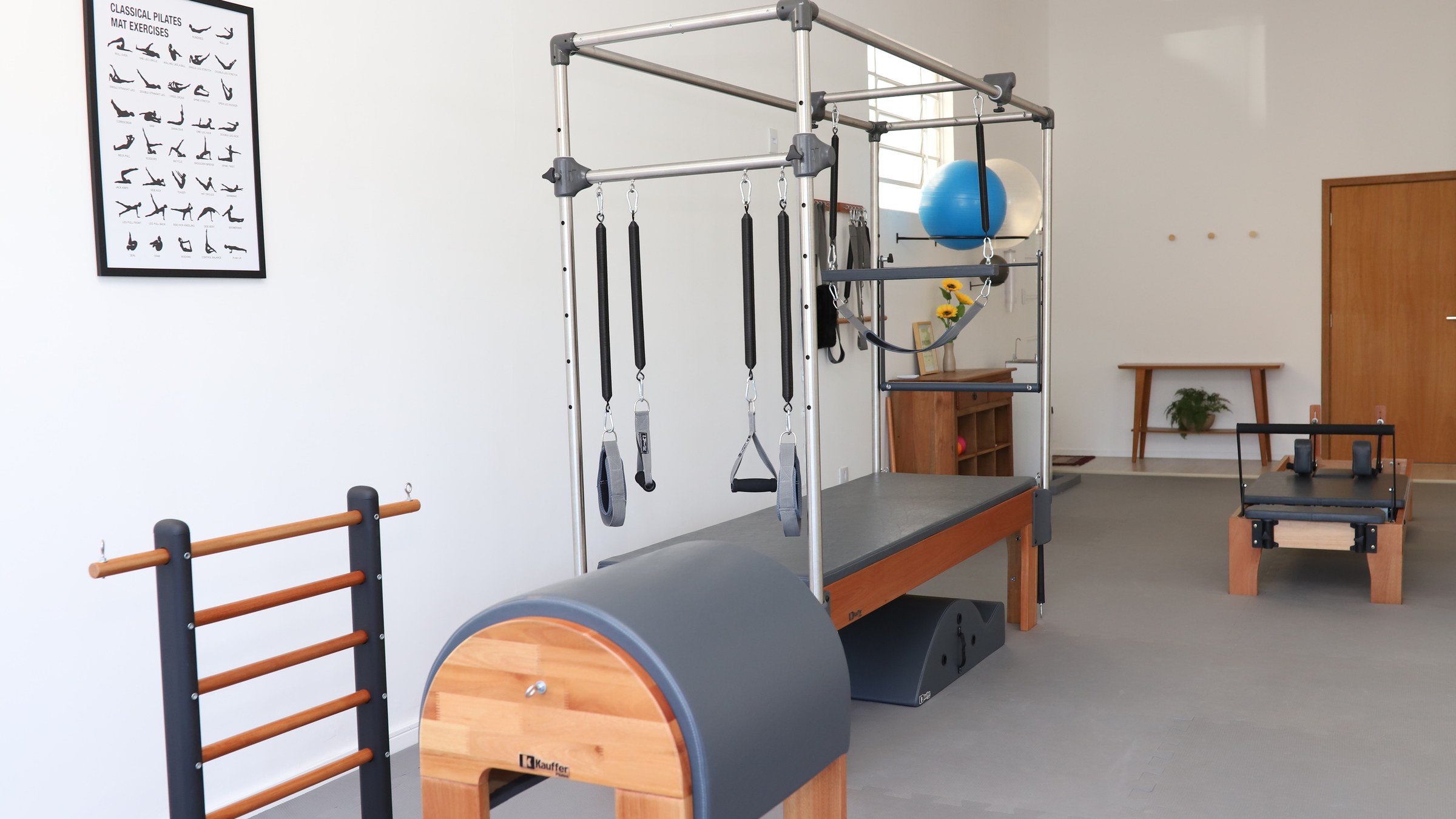 Sala de Pilates do Paola Studio com Cadillac, half barrel, escada e pôster Classical Pilates